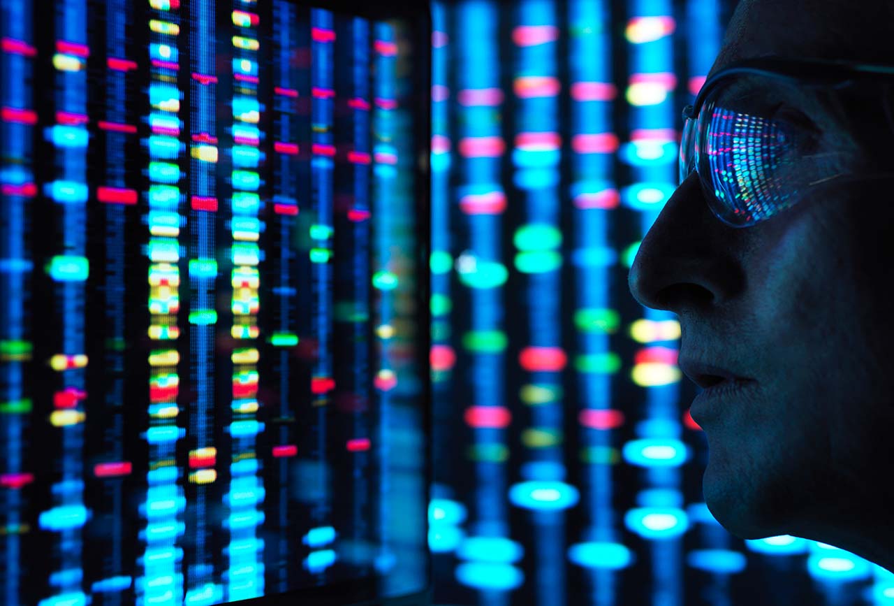 Scientist in glass next to a screen showing dna sequencing