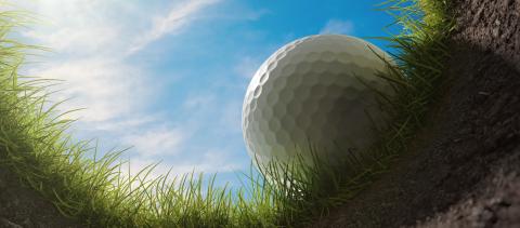 Looking up at a golf ball resting on the grass and soil, amongst blue skies